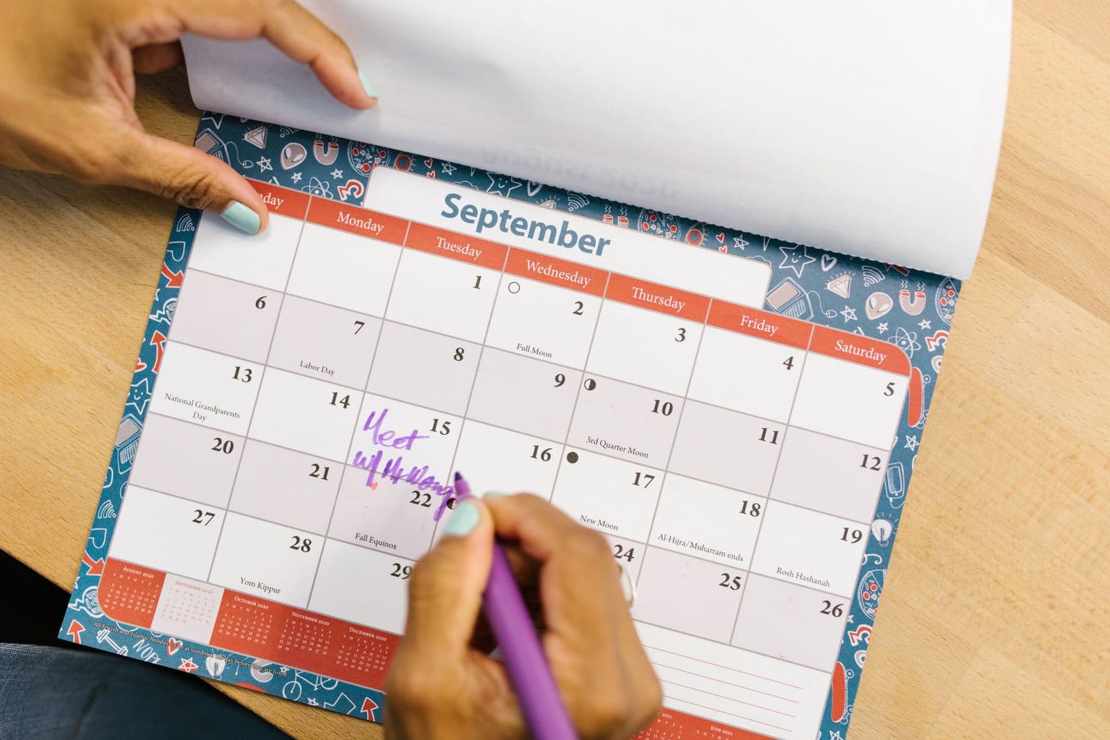 A hand marking a monthly planner calendar with a pen