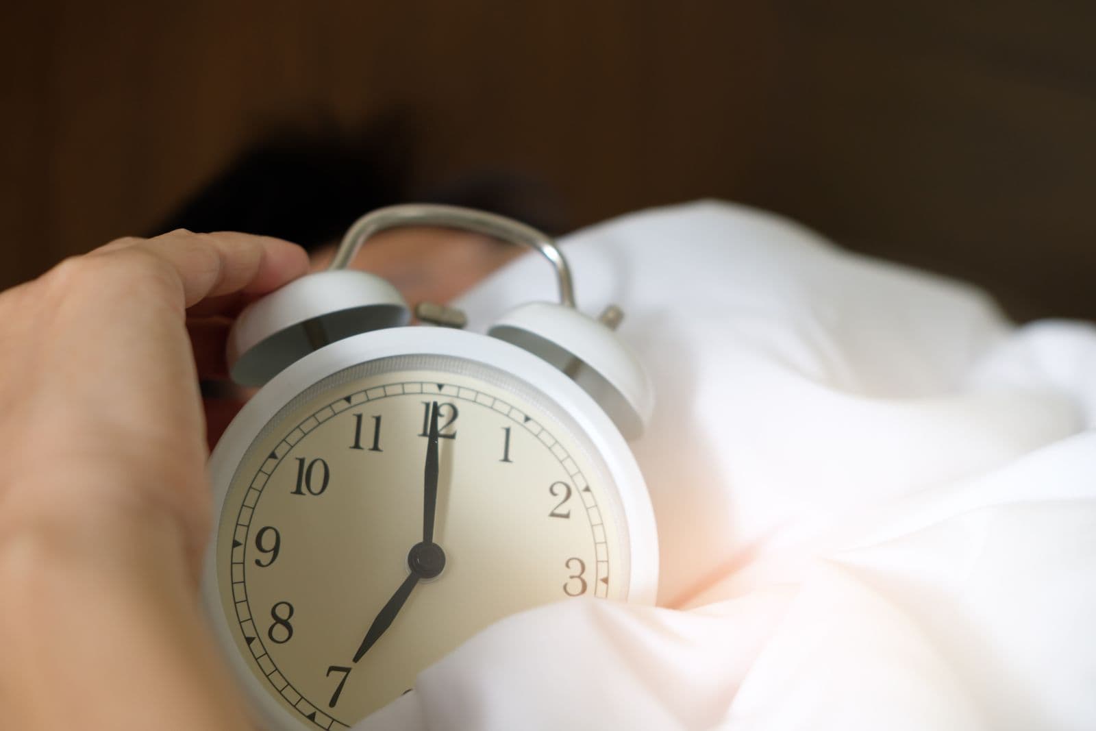 A hand reaching to switch off an alarm clock in the early morning