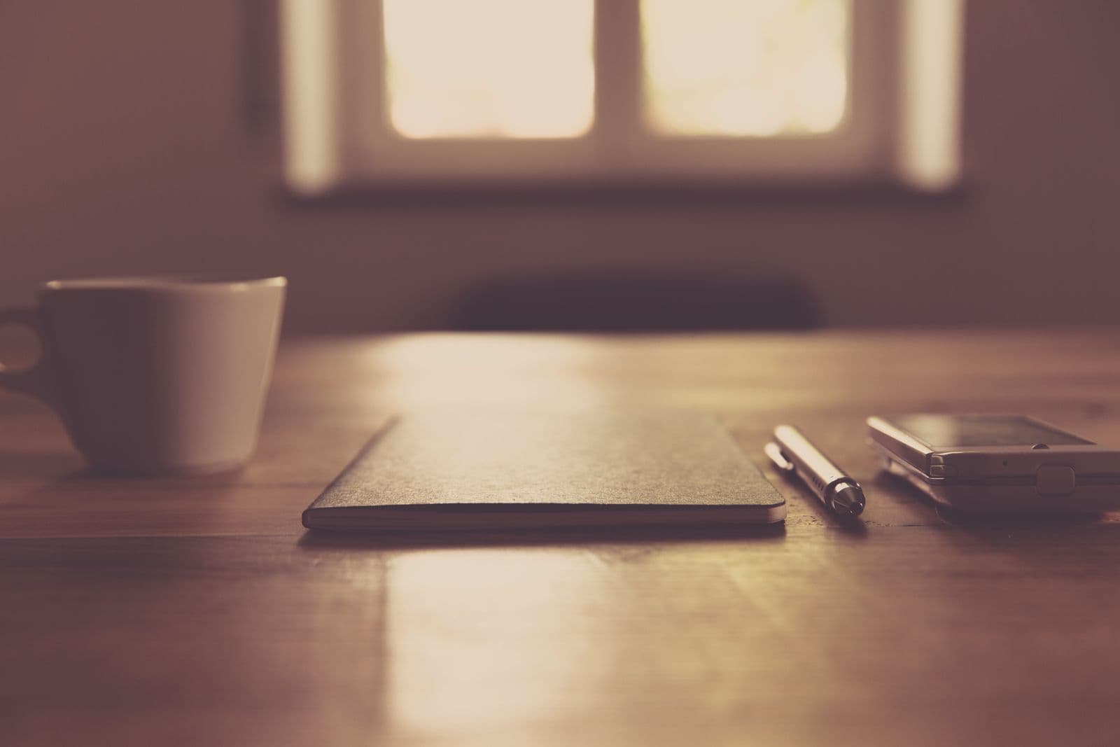 A warm morning desk with a closed notebook and a cup of coffee