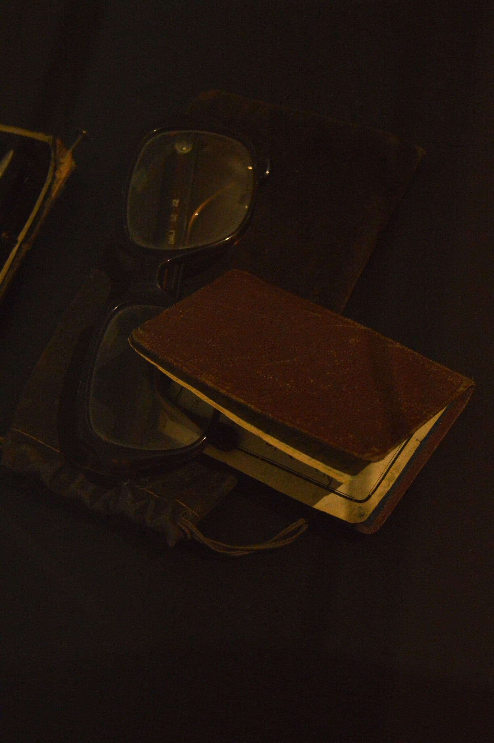 A closed leather notebook resting beside a pair of glasses in dim light